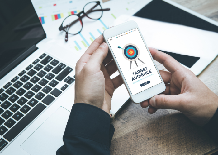 Image of a person holding a phone with an image on screen that says 'TARGET AUDIENCE' next to an illustration of a target.