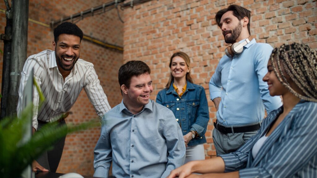 Five people in workwear chatting and laughing around a desk.