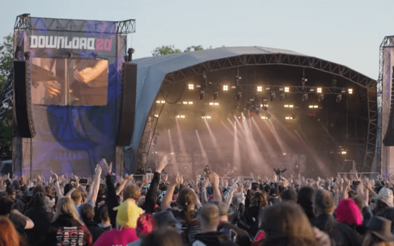 An image of a music festival with a big audience with their arms up in front of a big stage.