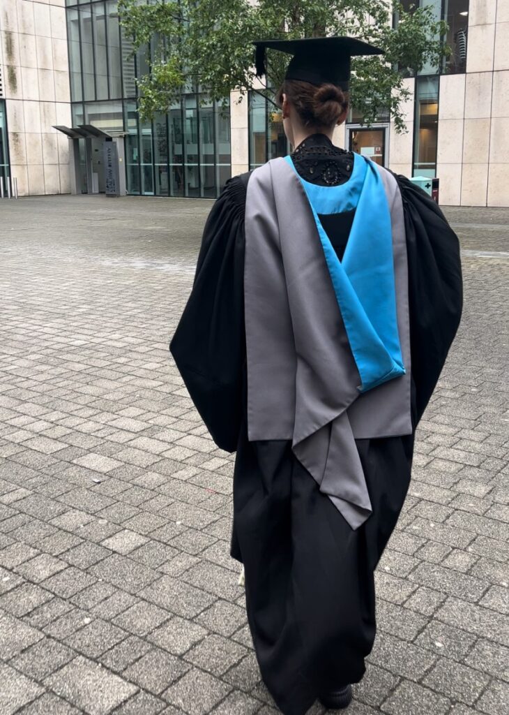 A picture taken from behind of Amy, a white brunette woman, with a graduation gown.