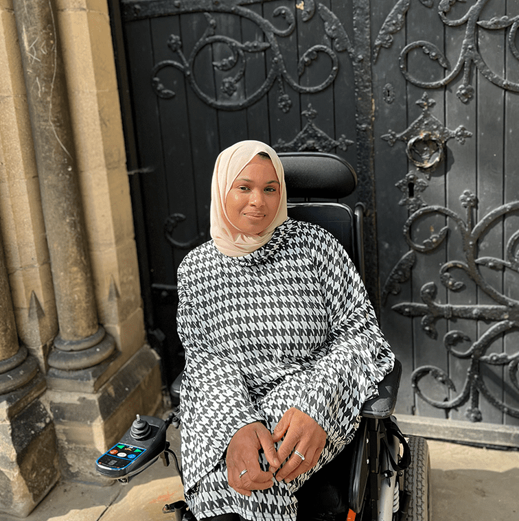 Umaymah poses in front of a large, old door surrounded by classic brickwork.