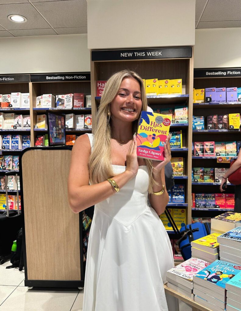 Tasha Ghouri smiles proudly in a bookshop holding up a copy of her new book.