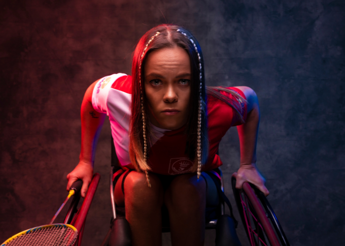 Woman in a wheelchair in a darkly lit room holding a tennis racket