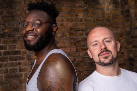 Chris Fonseca, a black man with short dark hair and glasses, is smiling to the camera and posing next to a white man.