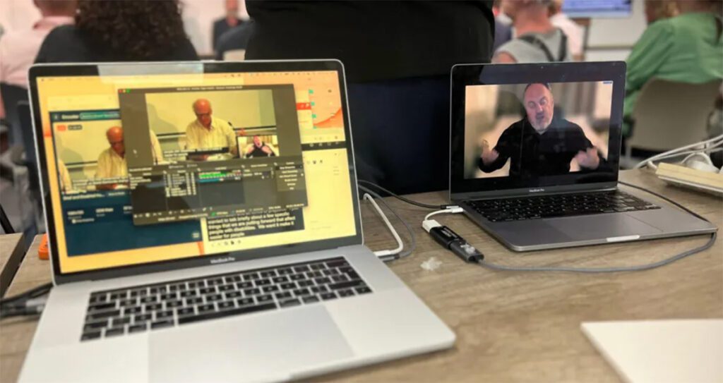 Laptops set up, live-streaming the political debate. There are several inclusivity features in place such as captions on the screen.