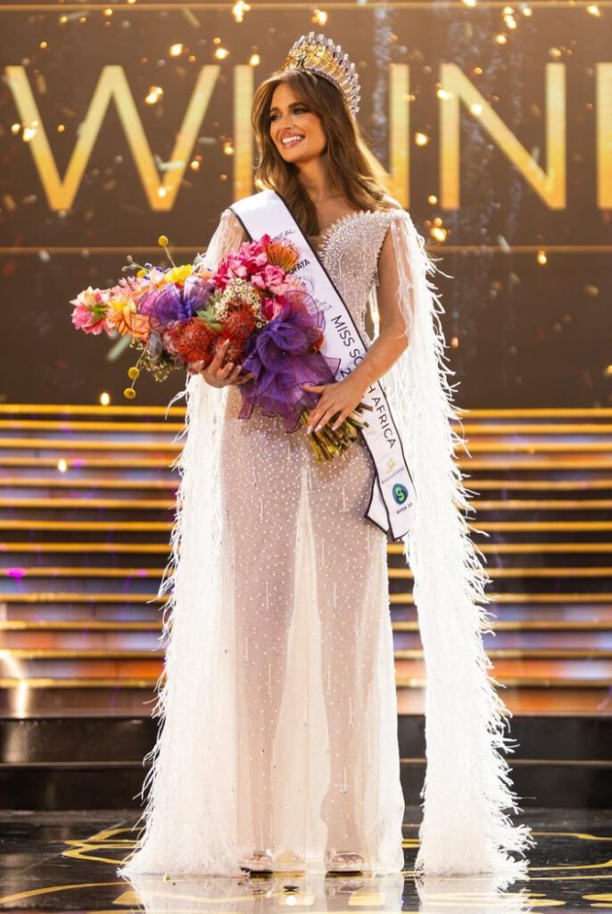 Mia le Roix after just being crowned Miss South Africa. She is holding the winner's bouquet and has the official sash over her shoulder.