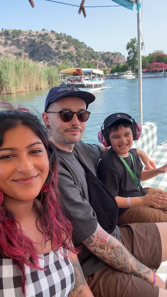 Yasmin sits on a river boat with her partner and child as part of a TUI holiday.