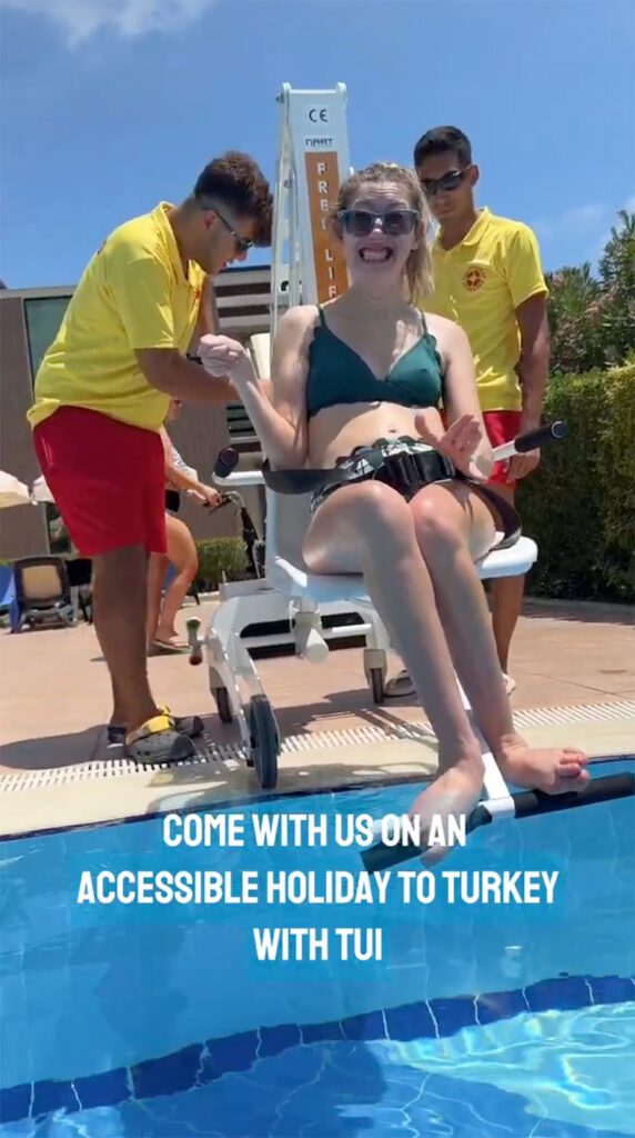 Hannah is grinning excitedly as she is lowered into a TUI pool using a pool lift. Caption on screen reads: "Come with us on an accessible holiday to Turkey with TUI."