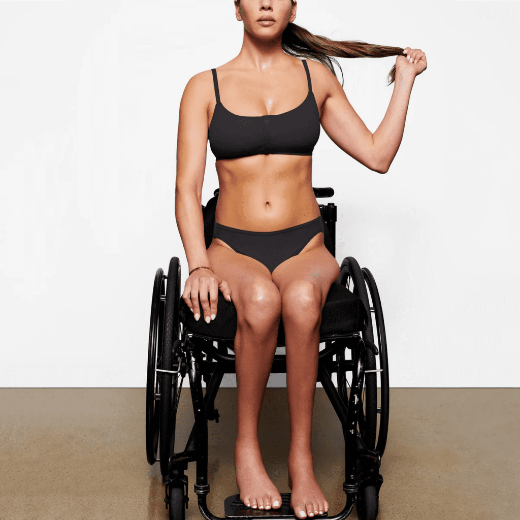 An image of a model on her wheelchair, posing with an adaptive underwear set from SKIMS.