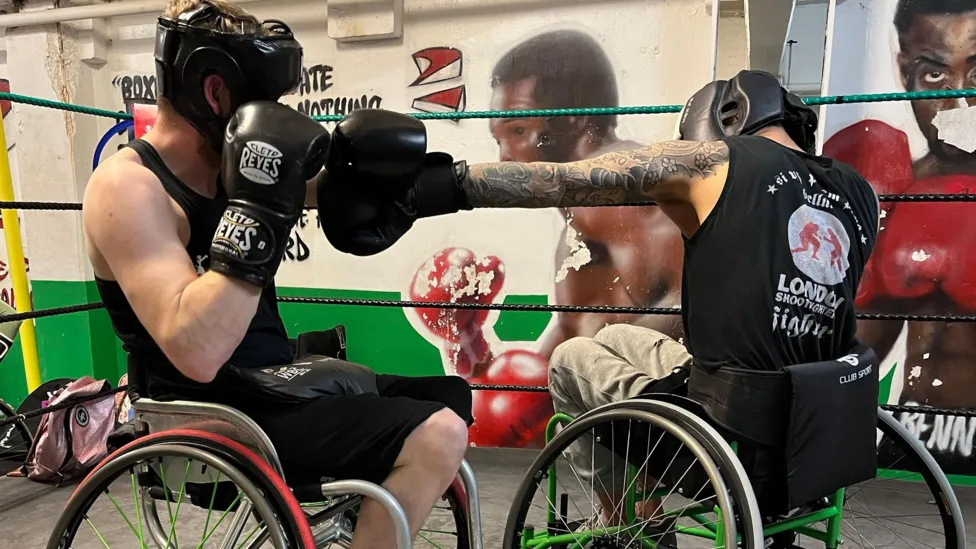 Two manual wheelchair users in a boxing ring, competing in an adaptive boxing match against each other.