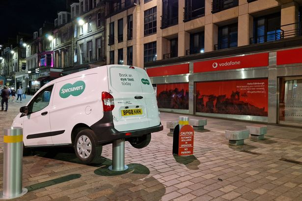 The rear of a Specsavers van rests on top of a rising bollard in an Edinburgh high street at night.