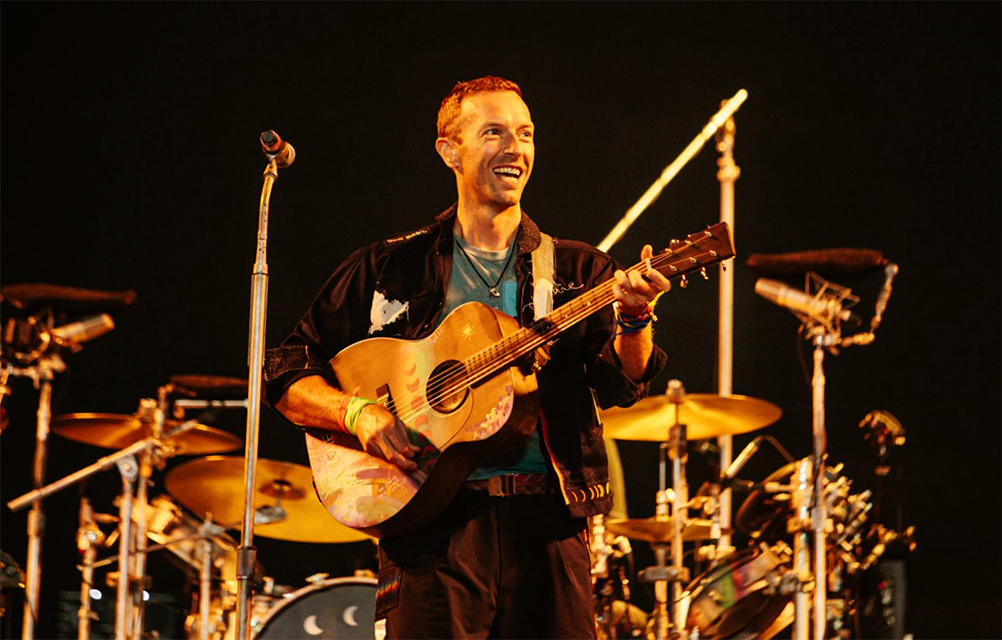 Chris Martin playing an acoustic guitar on stage at Glastonbury.